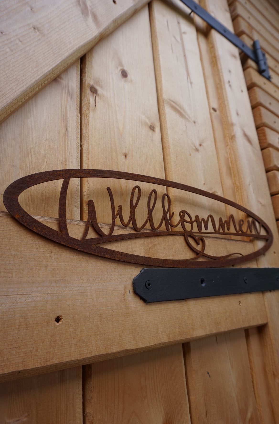 Edelrost Schild mit der Schrift Willkommen, hängt an einem Holztor