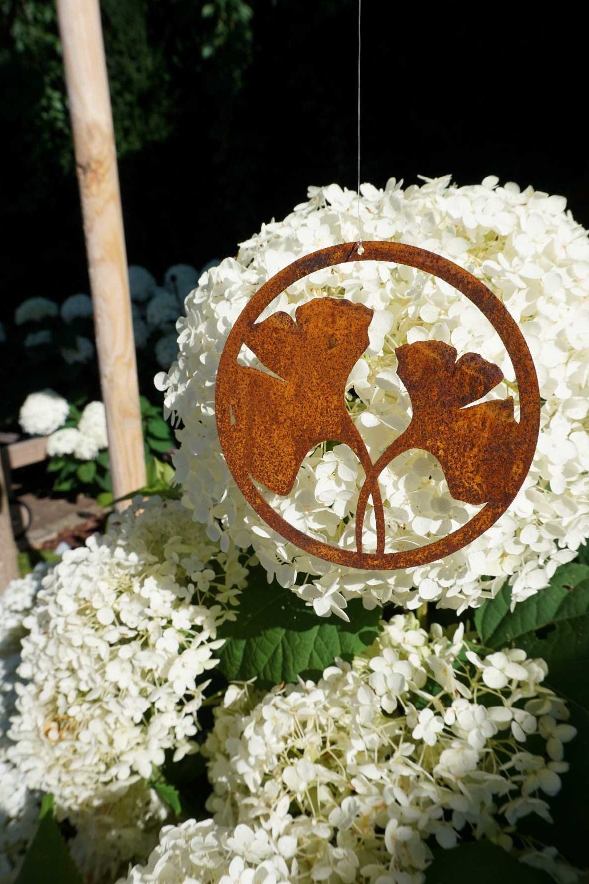 Edelrost Ginkoblatt vor einem Blumenbeet